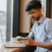 Indian student freelancer in a café, working on laptop with coffee, reading on phone