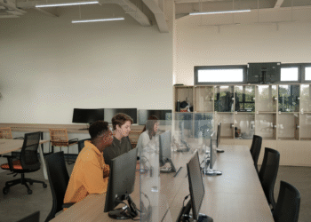 Modern open office workspace with diverse employees collaborating at desktop computers, representing a collaborative work environment.
