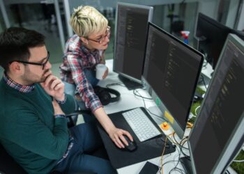 Senior and junior software engineers collaborating on computer screen, implementing best practices for building a robust alerting system.