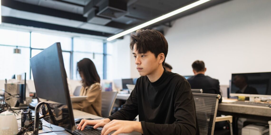 Young male PHP intern in black shirt focused on computer screen during internship. Implementing proven strategies for PHP internship success.