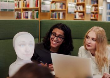 Two college friends studying in the library while reading about AI and ML internship strategies.
